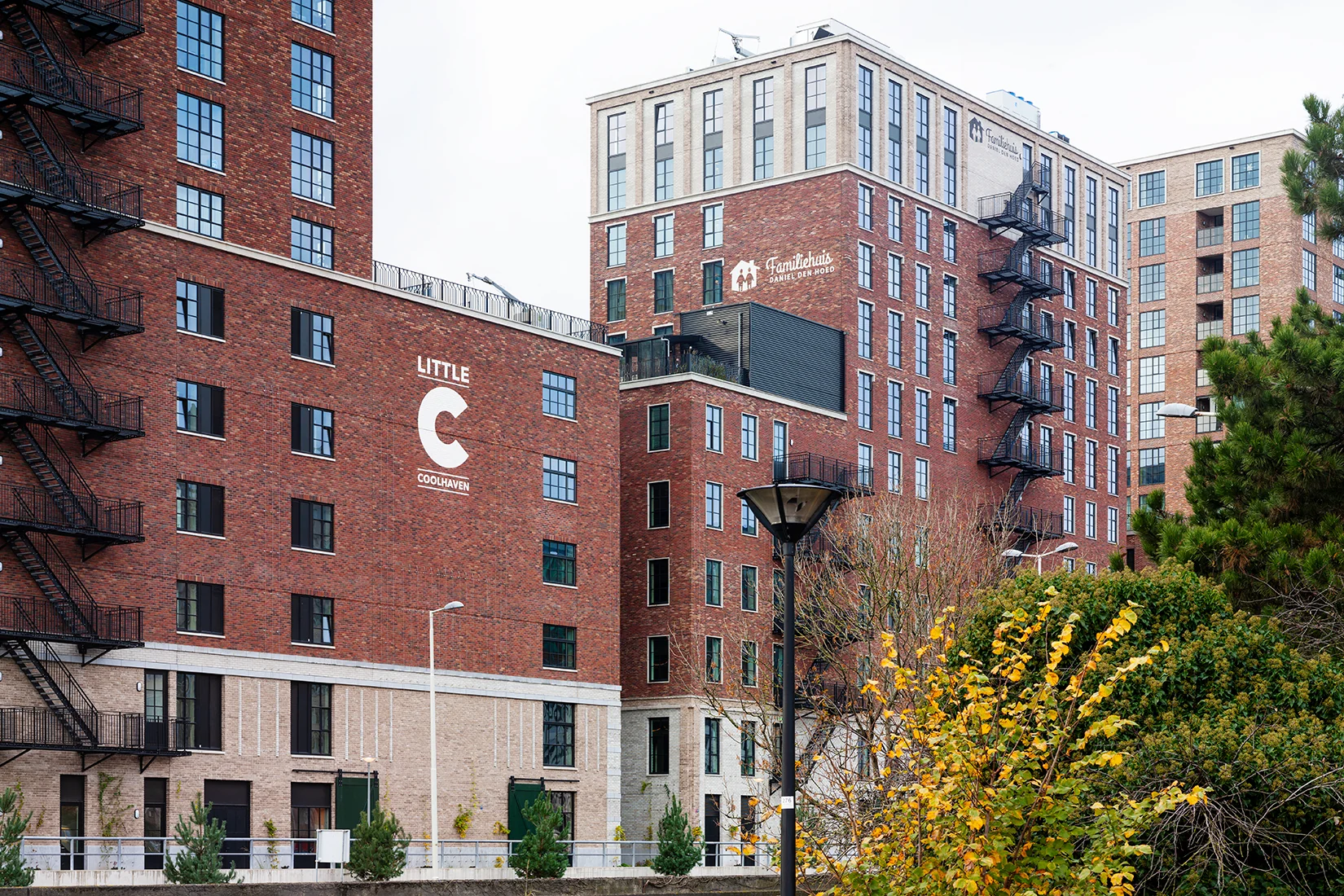 Rode bakstenen appartementencomplexen aan de Karl Weisbardstraat in Rotterdam, met de namen "Little C Coolhaven" en "Familiehuis Daniel den Hoed" op de gevels.